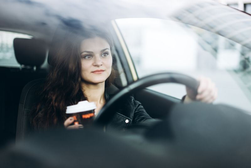 Woman driving her car with coffee in one hand